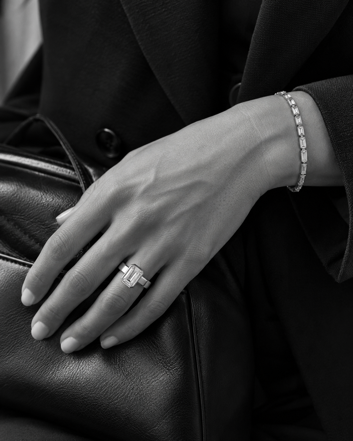 A modern platinum diamond ring and refined diamond bracelet worn with black tailoring and a leather bag